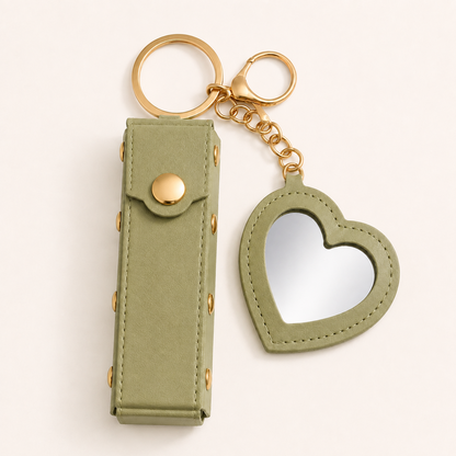 Black Lipstick Holder and Mini Heart Mirror Keychain with gold hardware on a clean light background